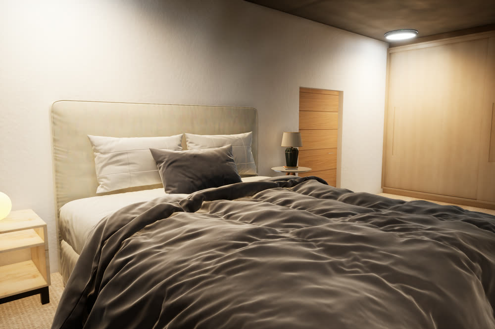 Bedroom with a double bed in grey linen, a glowing bedside lamp and wooden wardrobe doors.